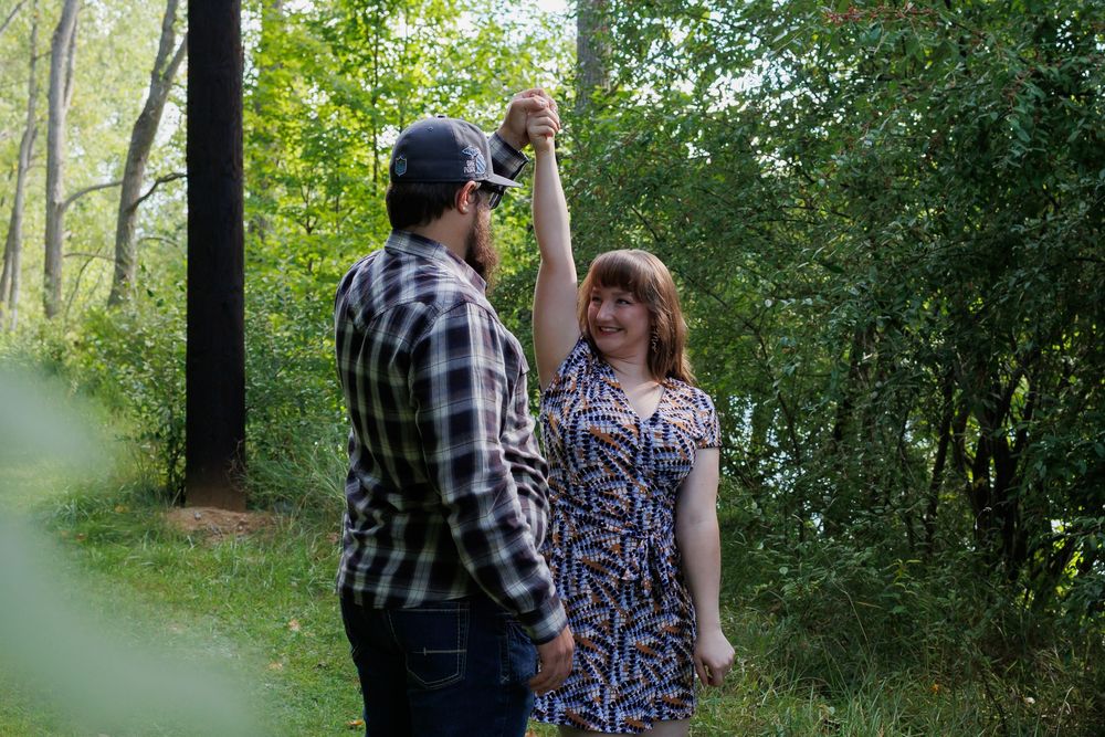 A couple shares a romantic moment together while walking through a lush green forest path.