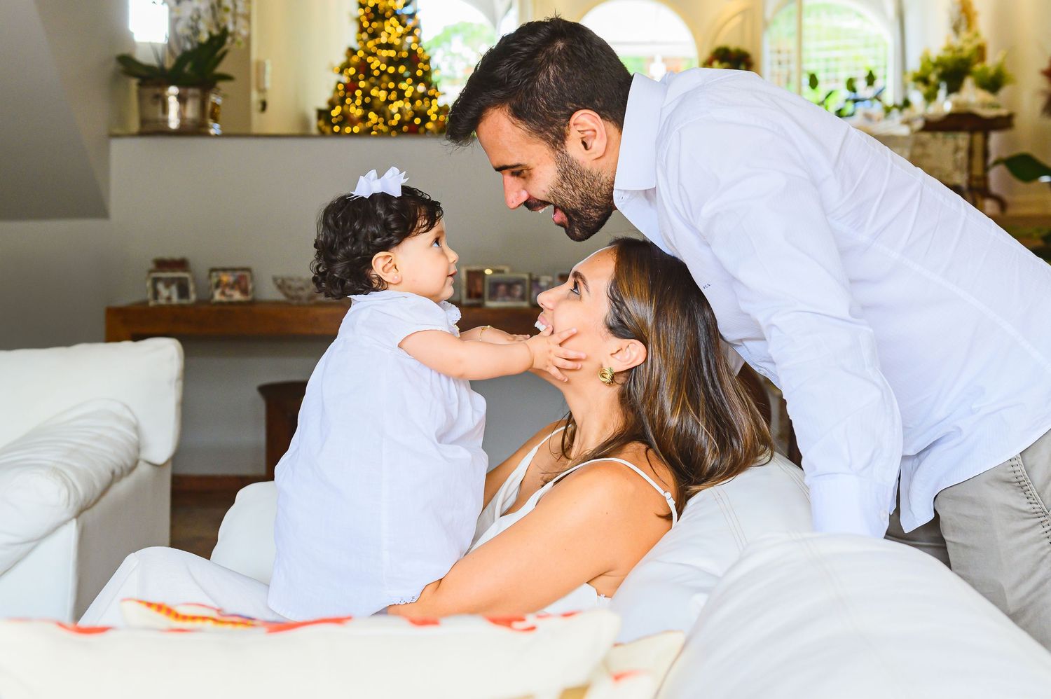 Family sharing a tender moment together on a white couch with a Christmas tree visible in the background.