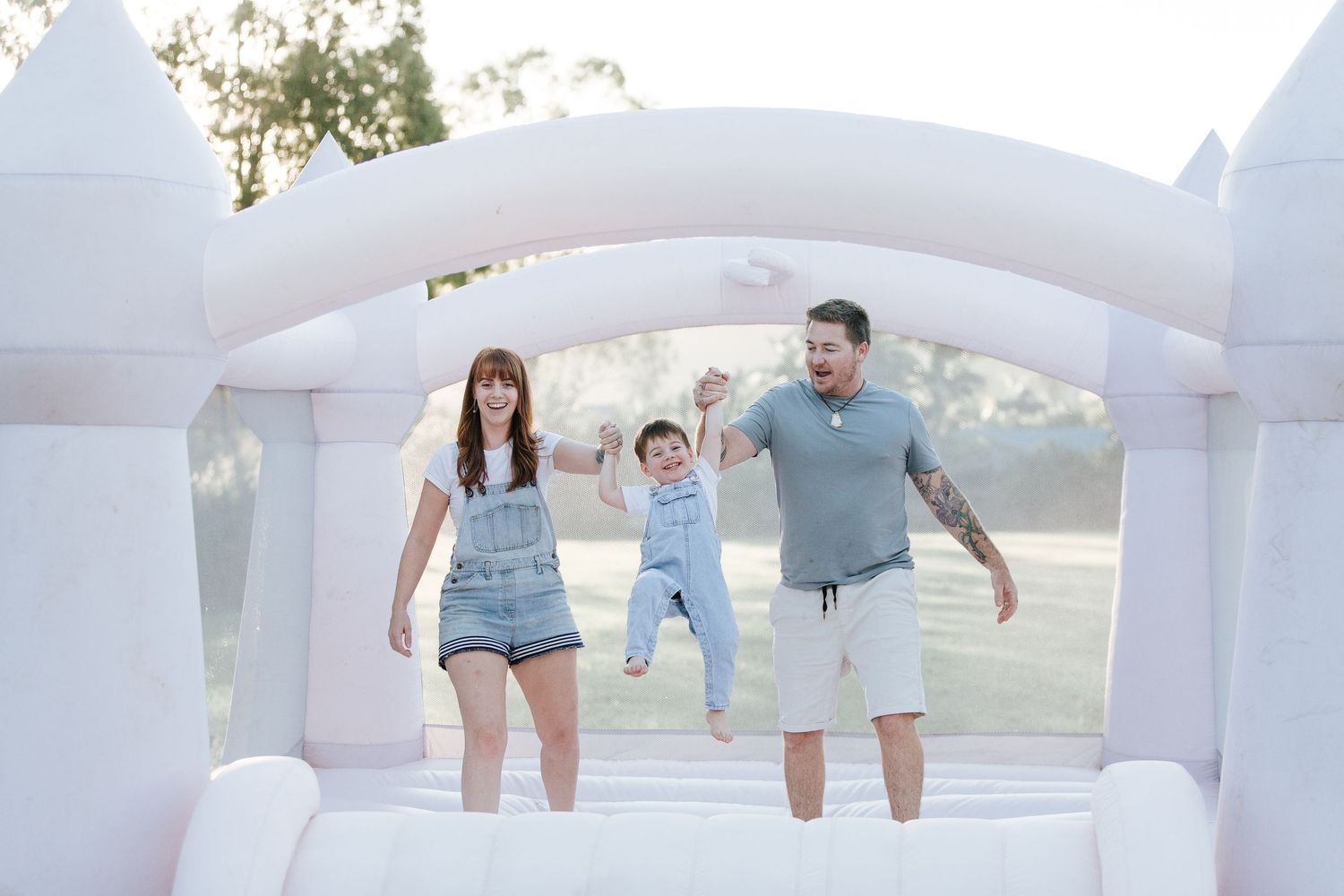 A family bouncing together in a white inflatable castle on a sunny day.
