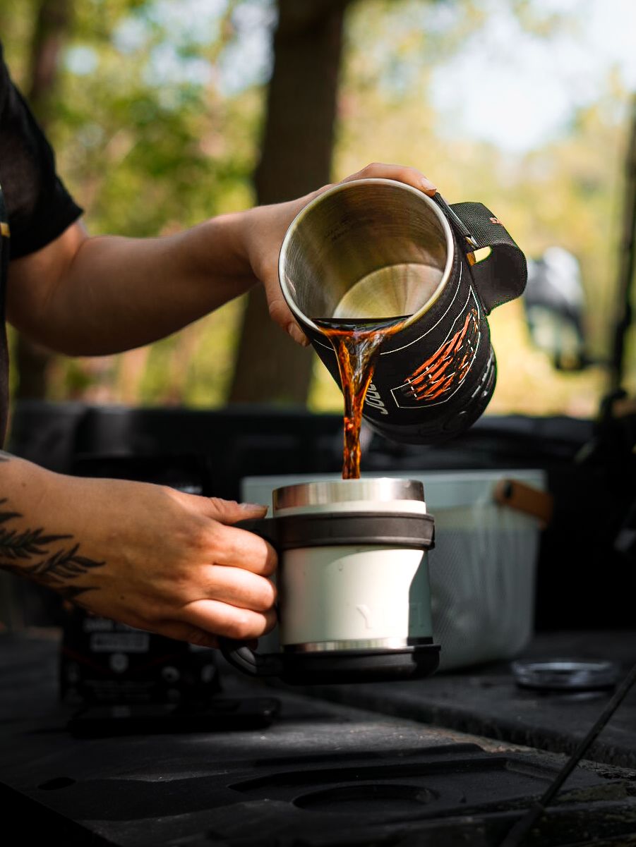 Hands preparing coffee with black branded cups on wooden surface.