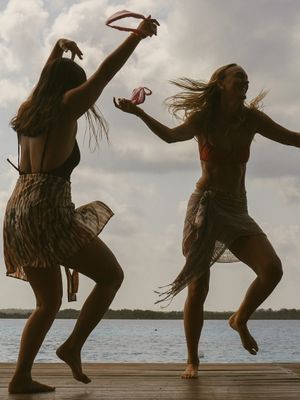 Two carefree dancers leaping joyfully on wooden dock at sunset.