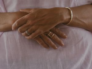 Close-up of hands with rings resting on white fabric.