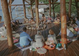 Large group gathered for yoga or meditation session on a covered oceanfront deck.
