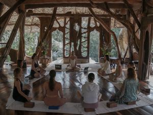 A group meditates in a circular formation inside a wooden pavilion during a wellness retreat.