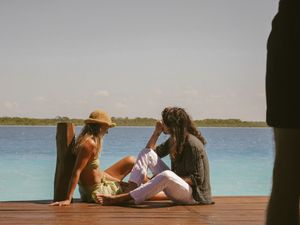Friends relaxing on wooden dock overlooking crystal blue waters on sunny day.