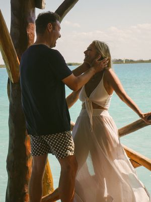 Couple sharing romantic moment on wooden deck overlooking turquoise waters.