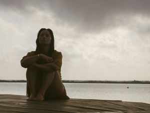 Silhouetted figure sits contemplatively on dock overlooking water at dusk.