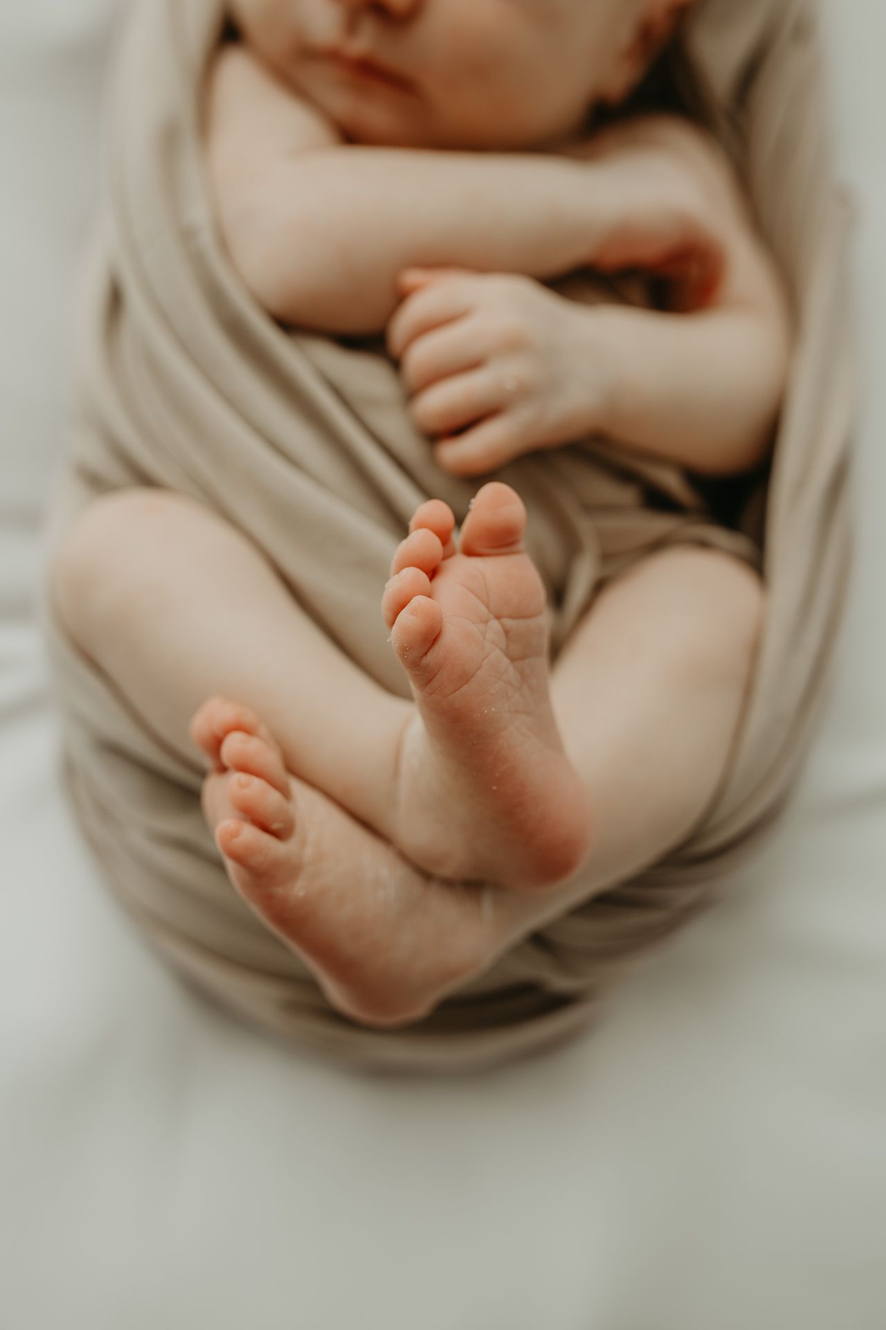 Close up view of tiny baby feet and legs wrapped in a soft beige blanket against white bedding.