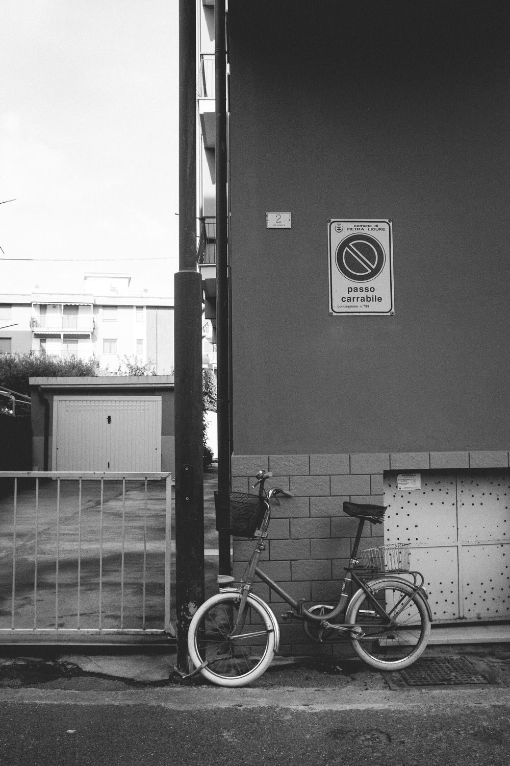 A vintage bicycle parked against a concrete wall with a no parking sign in black and white photography.