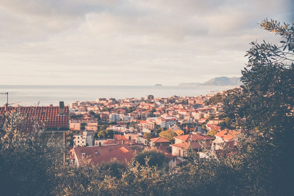 View over red-tiled rooftops of a Mediterranean hillside town during golden hour with tree branch in foreground.
