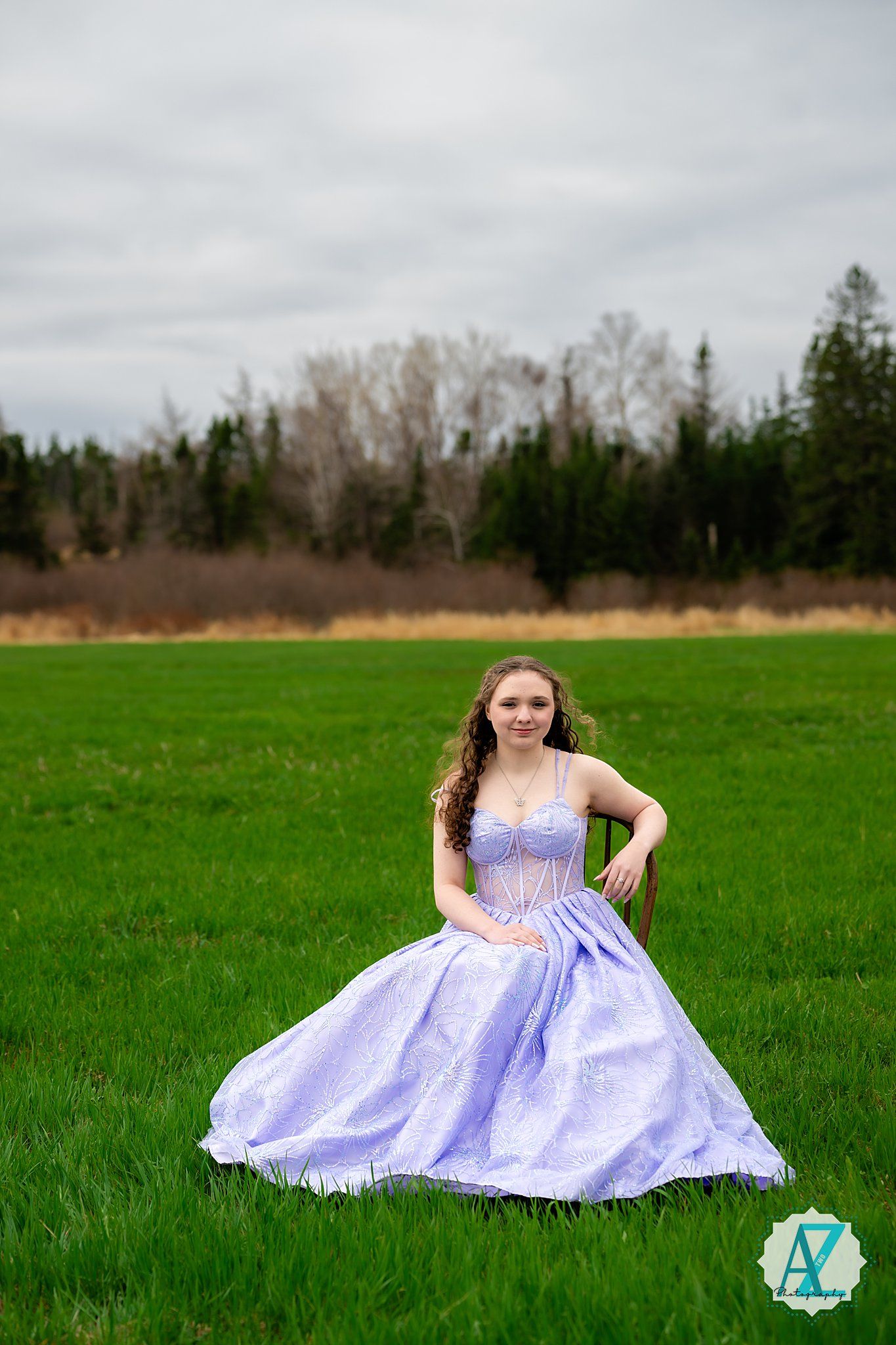 A purple and lavender ballgown with sparkles flows gracefully across a vibrant green spring meadow on an overcast day.