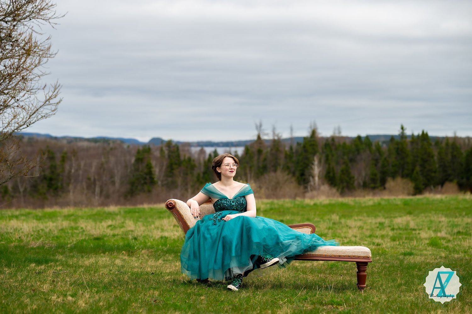 Elegant green dress flows across rustic wooden bench in scenic mountain meadow under cloudy skies.