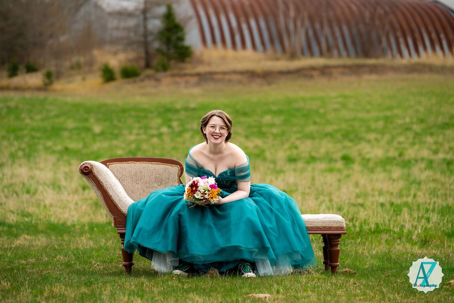 A teal ballgown adorns an antique bench in a peaceful countryside setting.
