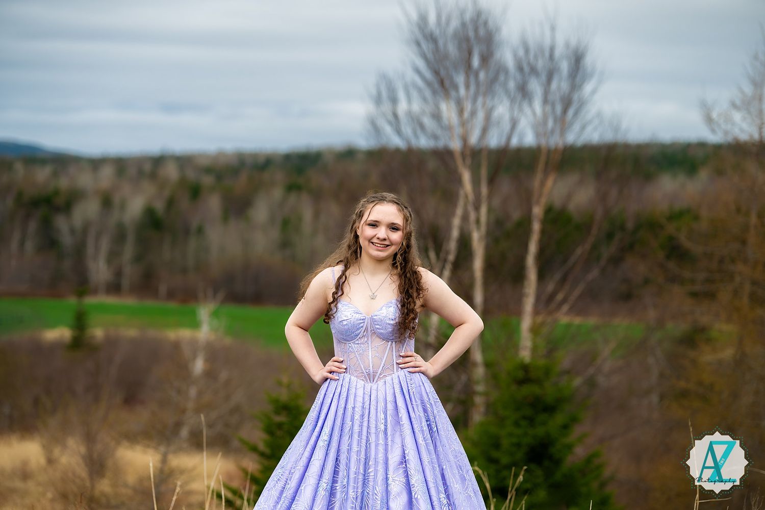 A lavender princess gown stands out against the natural landscape of rolling hills and bare trees.