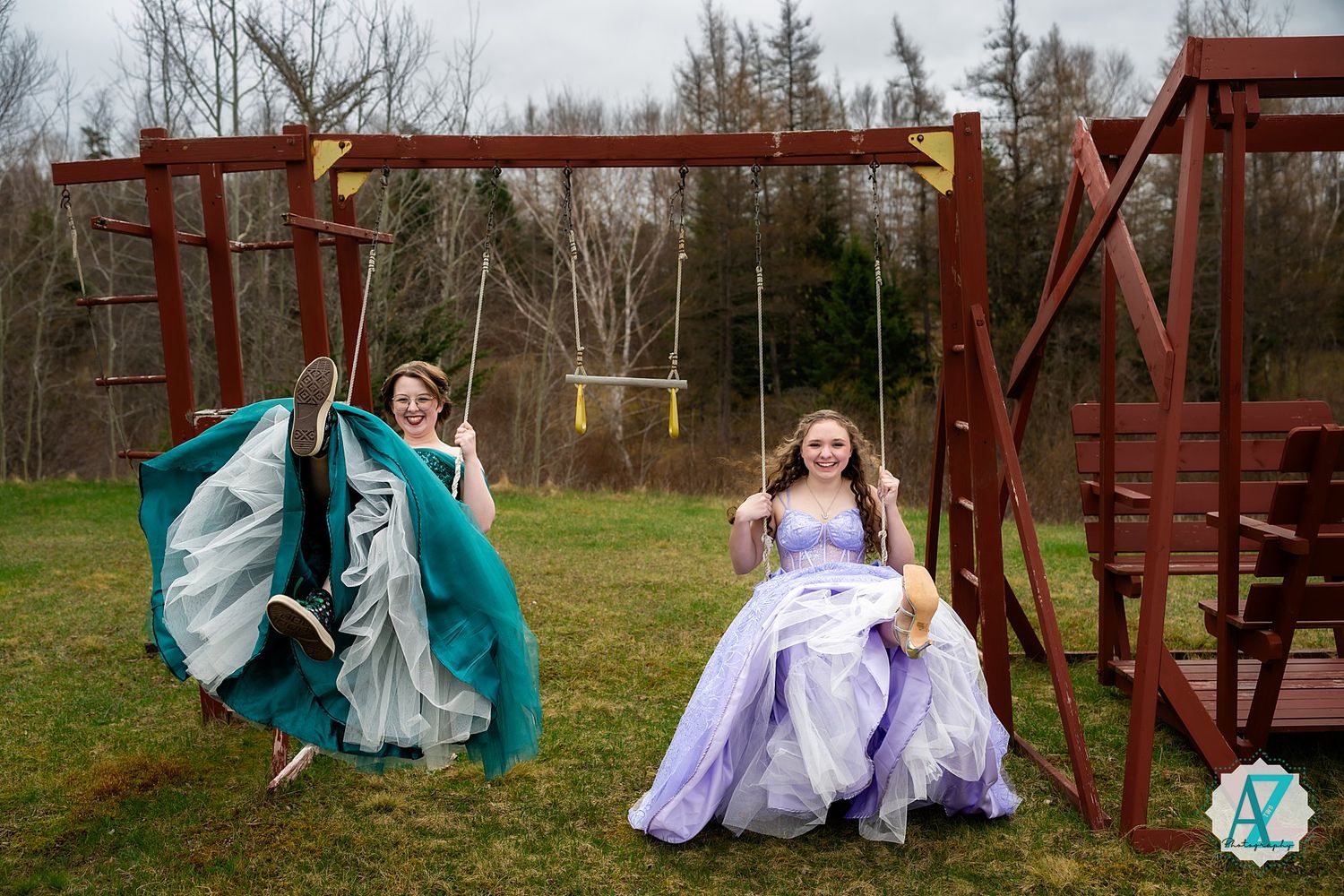 Two ballgowns, one teal and one lavender, create a playful scene at a rustic playground set.