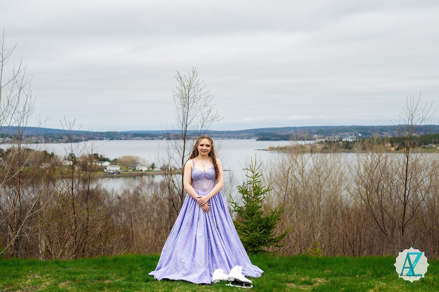 A person in a flowing lavender gown poses on a hilltop overlooking a scenic lake landscape.