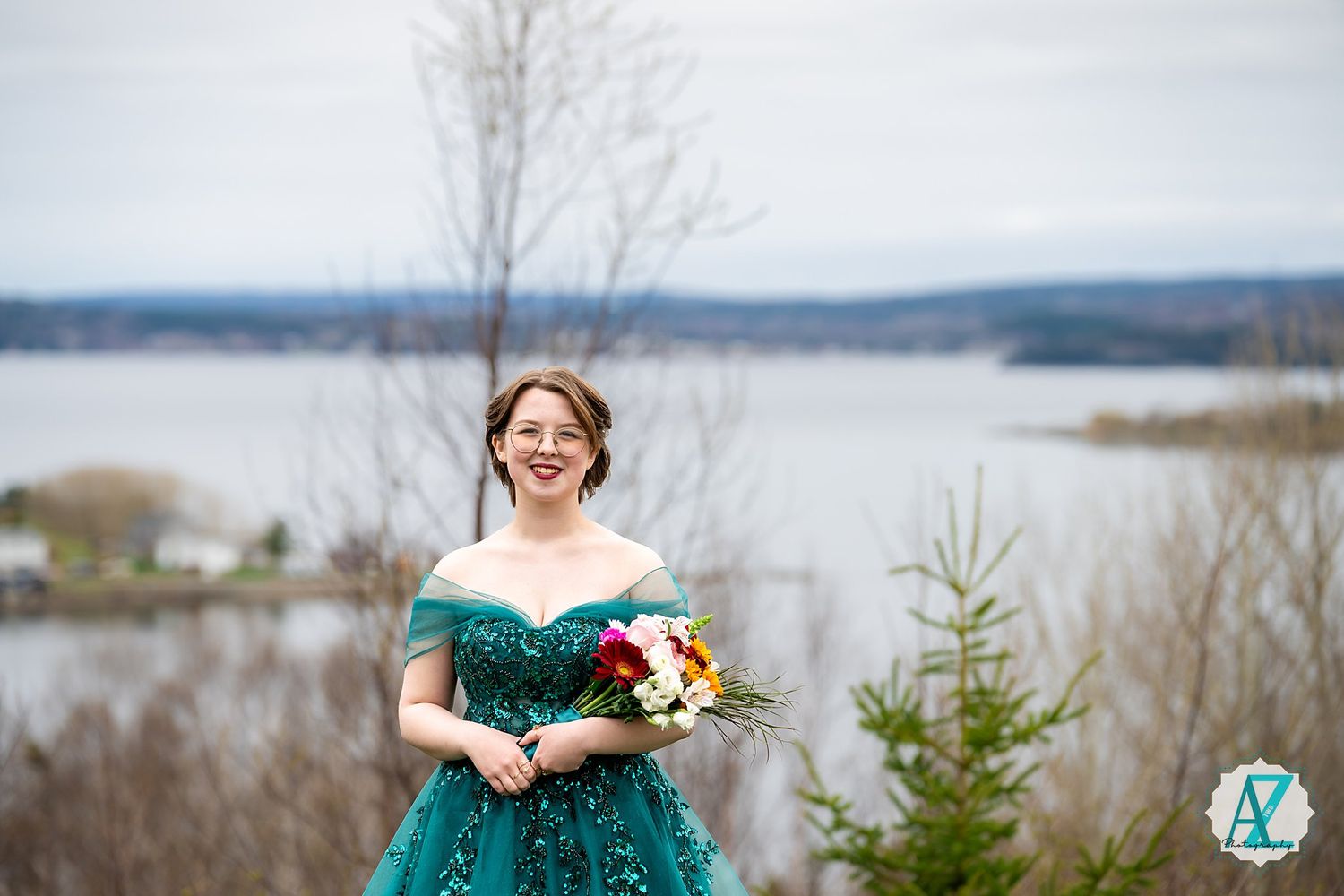 A figure in a sparkly emerald green gown holds a bouquet against a scenic lake backdrop.
