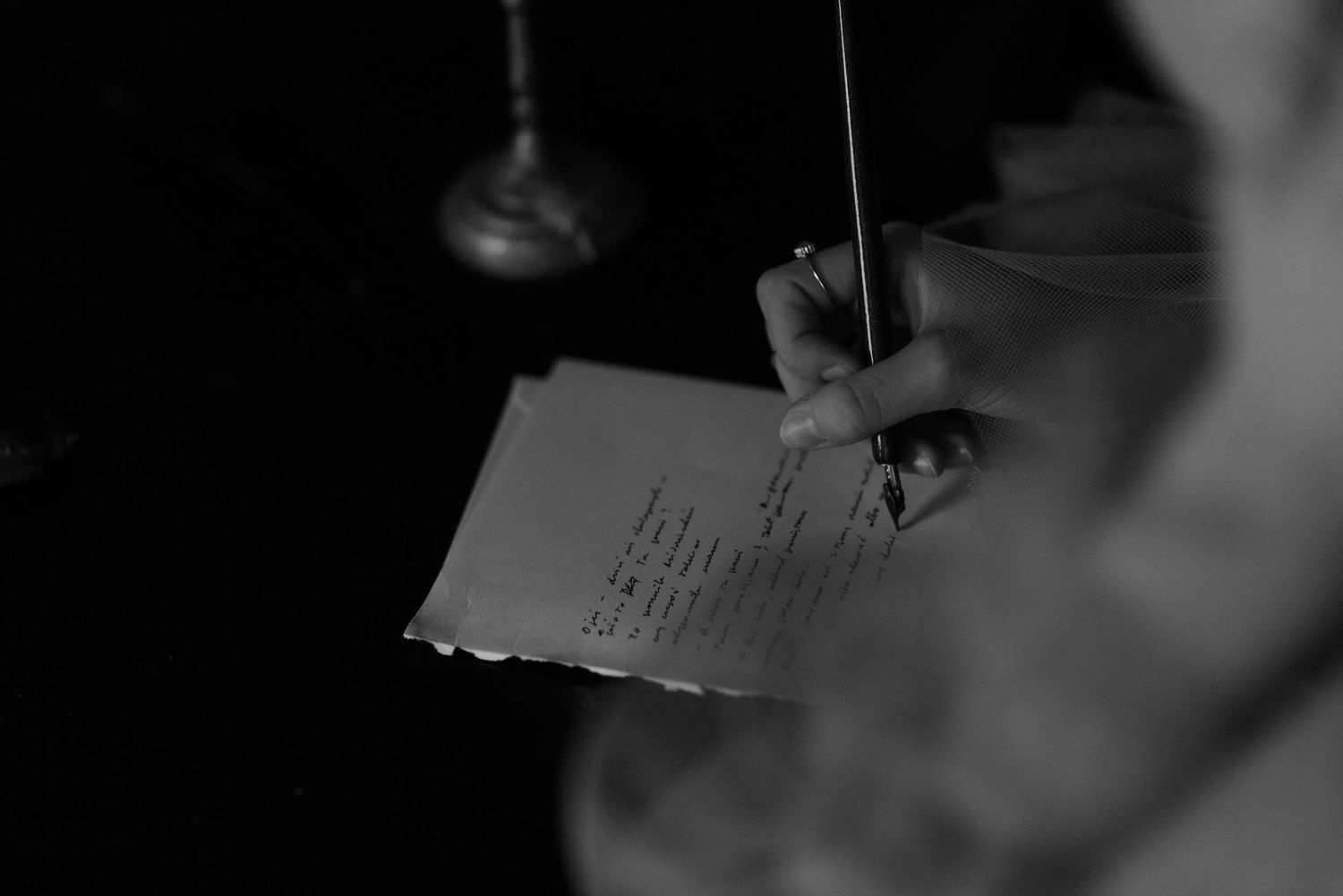 Someone writing on paper in a dark environment while grasping a pen or pencil.