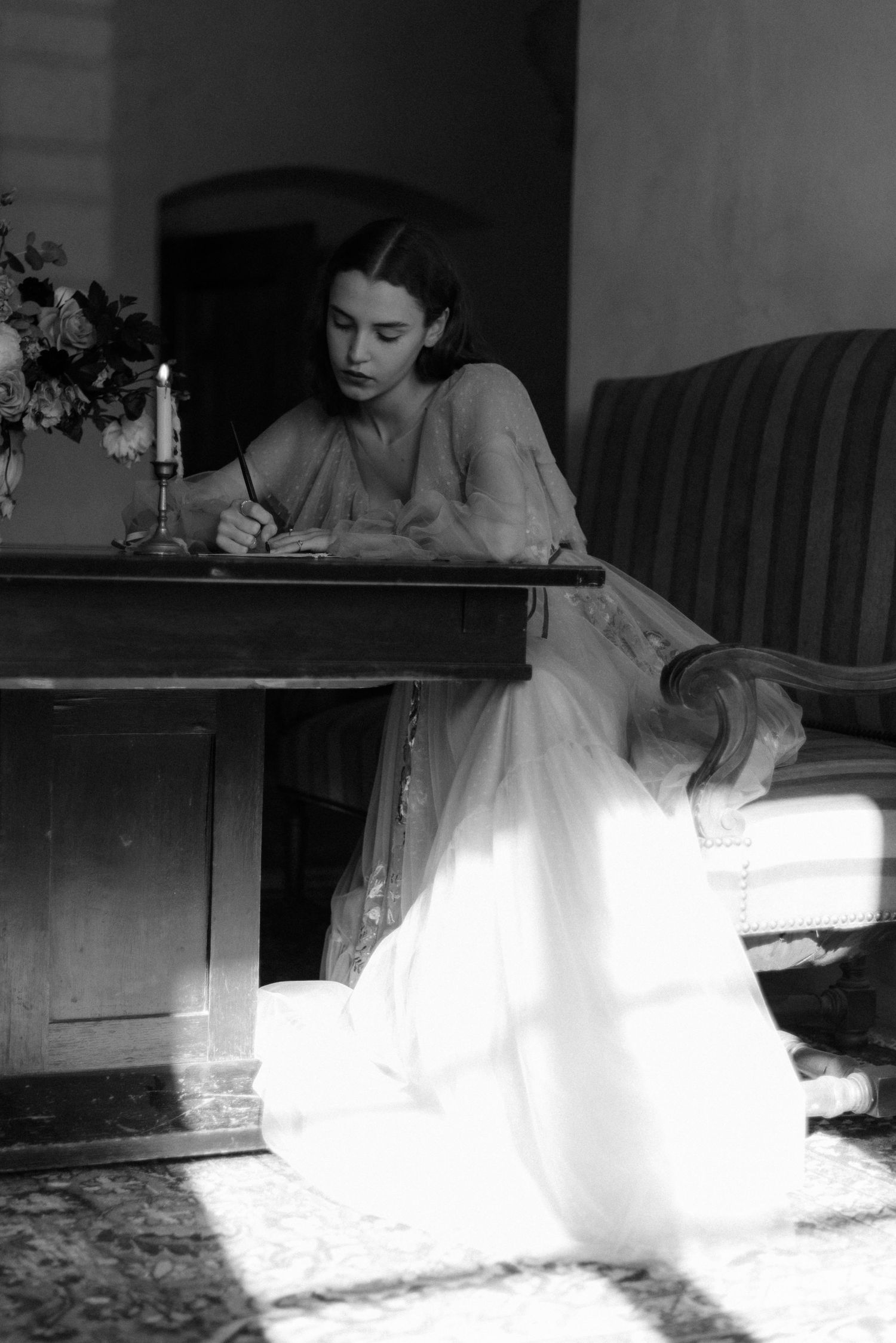A vintage black and white photograph shows someone writing at a desk with a candlestick, creating an atmospheric scene.
