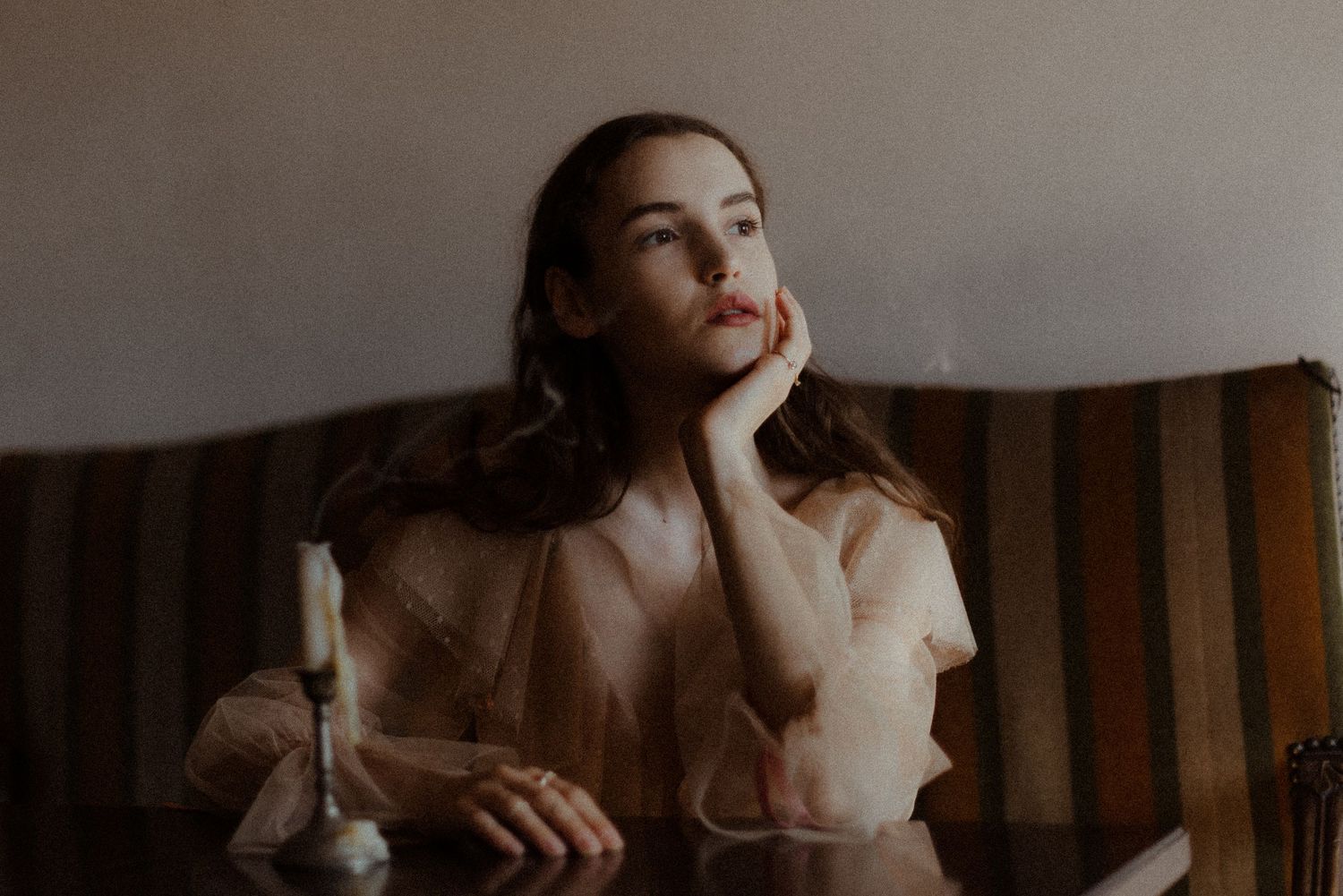 A dreamy portrait of a woman in vintage style sitting by a window in soft natural lighting.