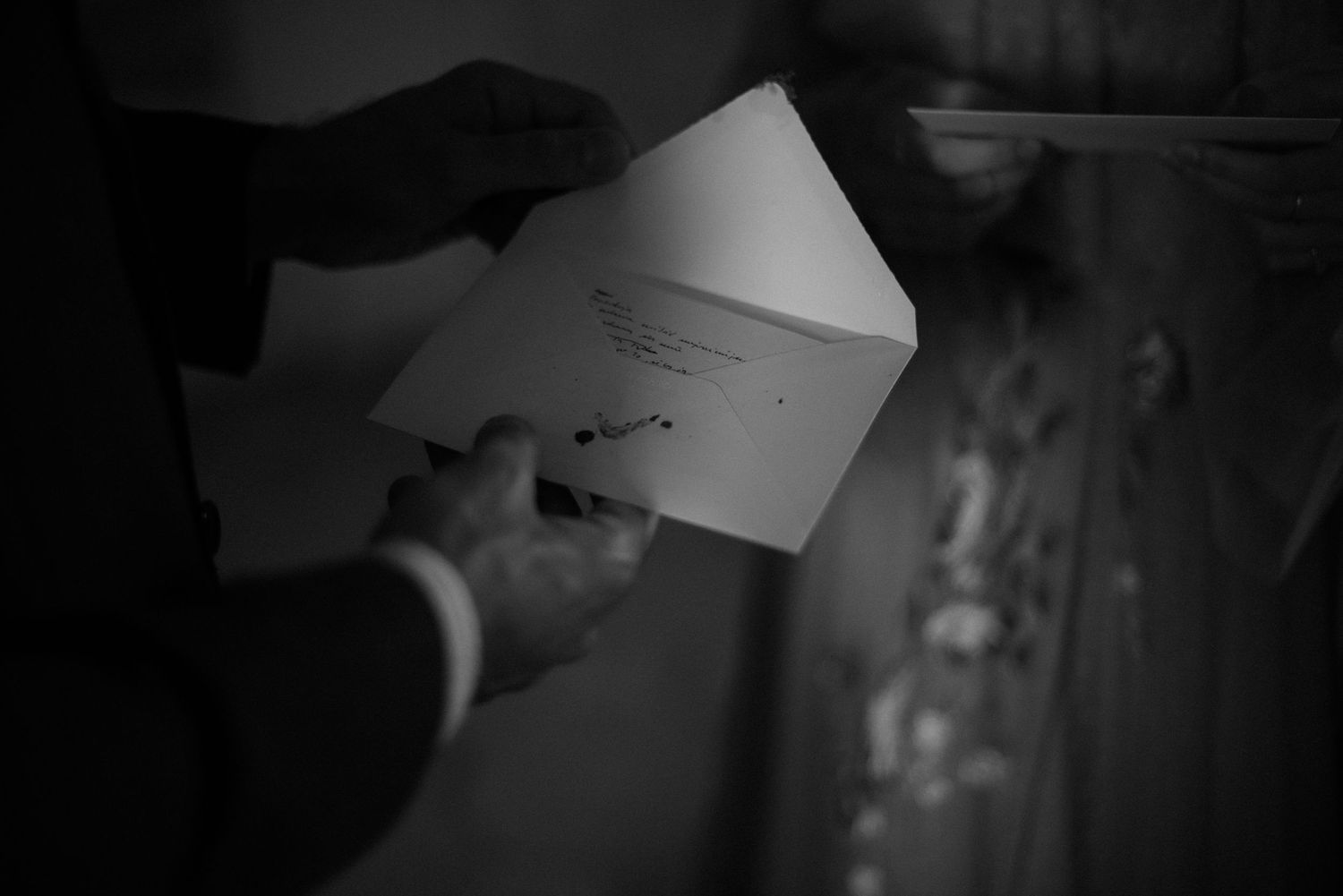 A hand holds a white envelope in a dimly lit black and white scene.