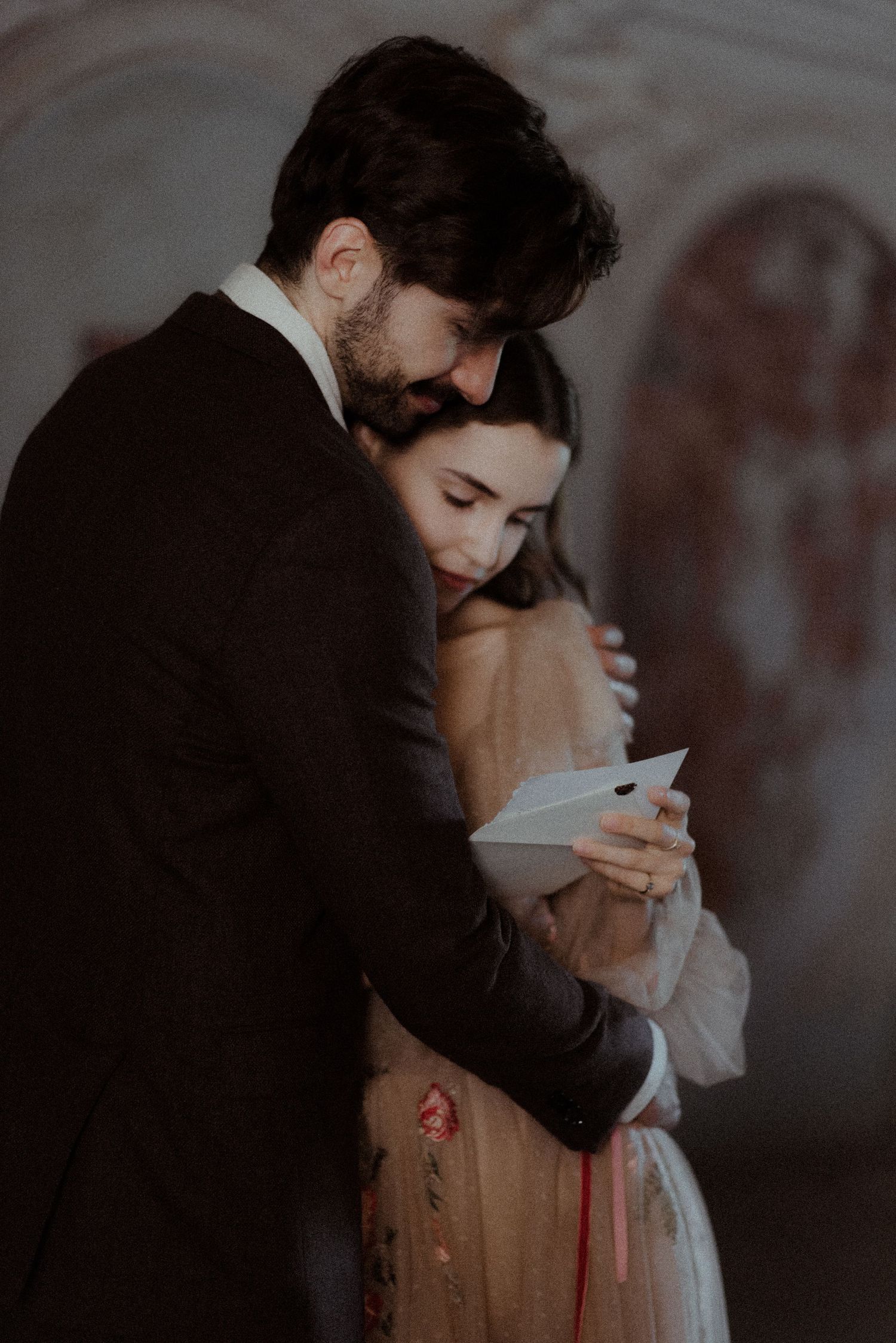 A romantic moody wedding portrait of a couple in formal attire sharing an intimate moment while looking at a phone.