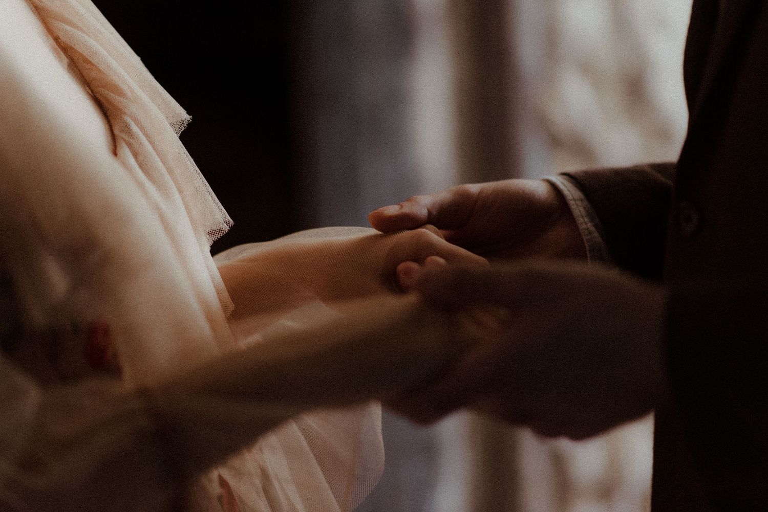 Two hands gently touch and hold each other in an intimate moment against a soft blurred background.