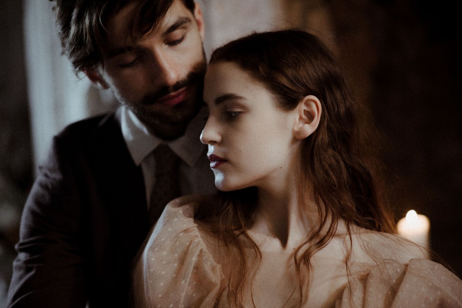 Moody and romantic portrait of a couple in vintage-inspired attire illuminated by soft candlelight.