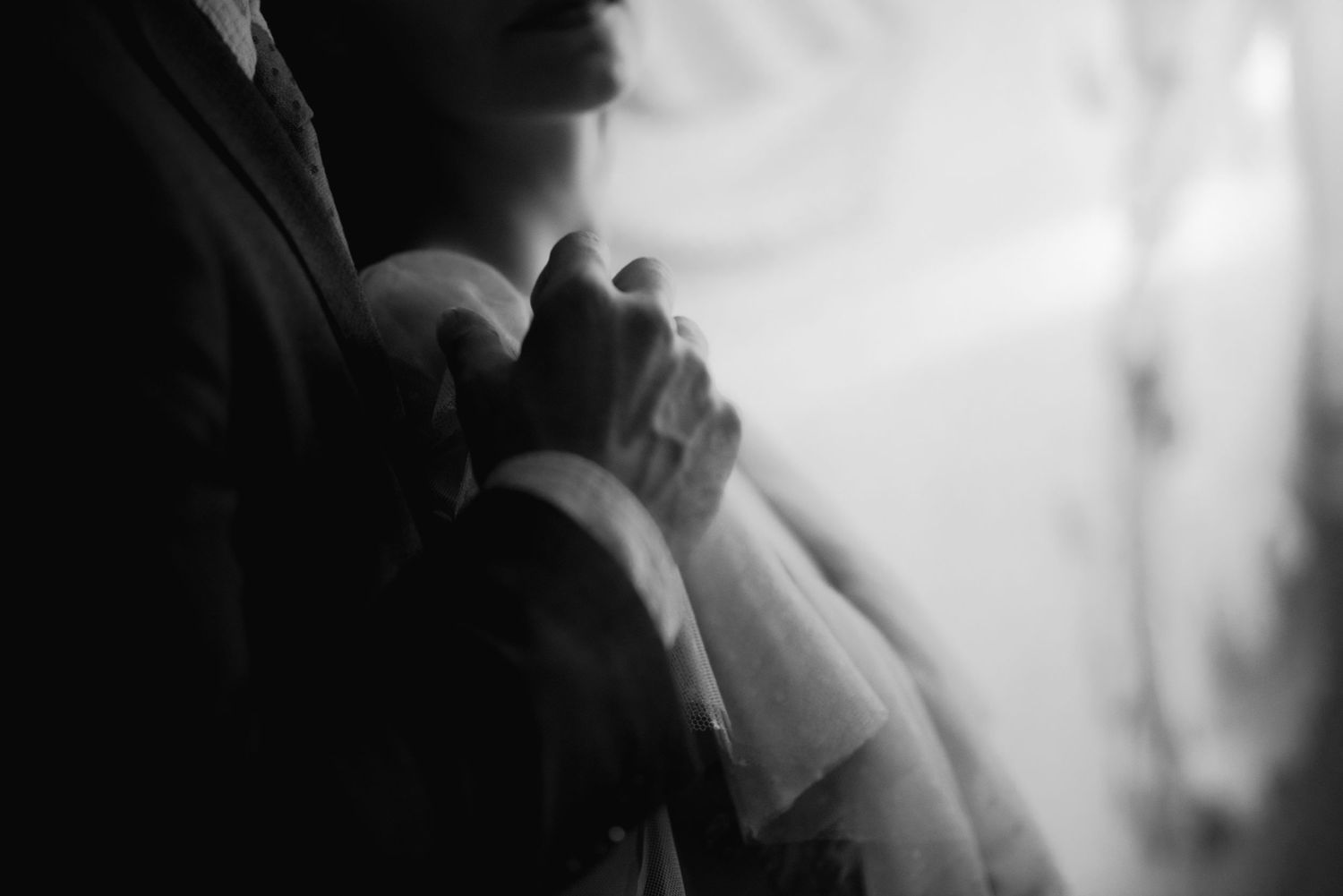 A black and white photo shows two embracing figures in formalwear with soft lighting and romantic atmosphere.