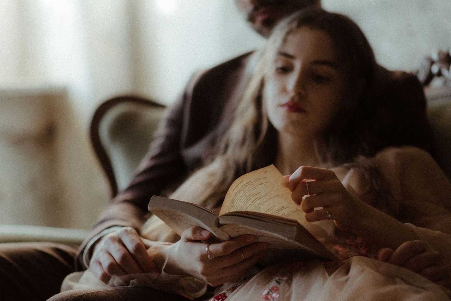 Person reading a book while relaxing on a couch in a softly lit room.