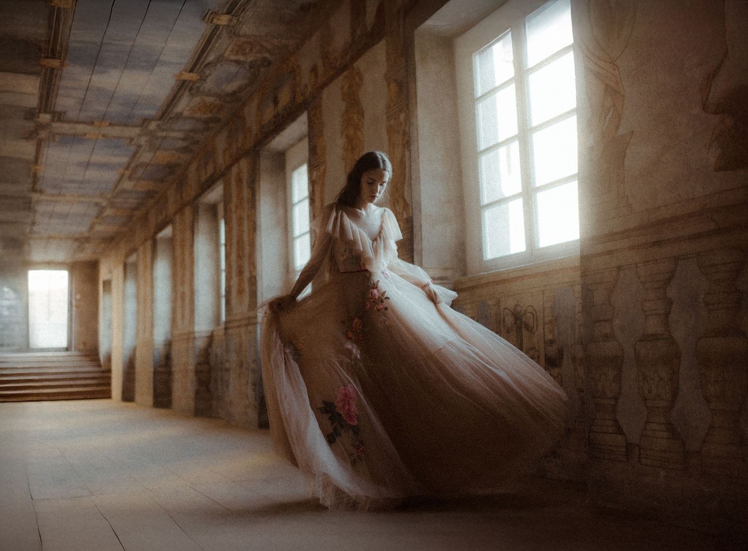 A flowing white wedding dress twirls elegantly in a sunlit stone hallway with tall windows.