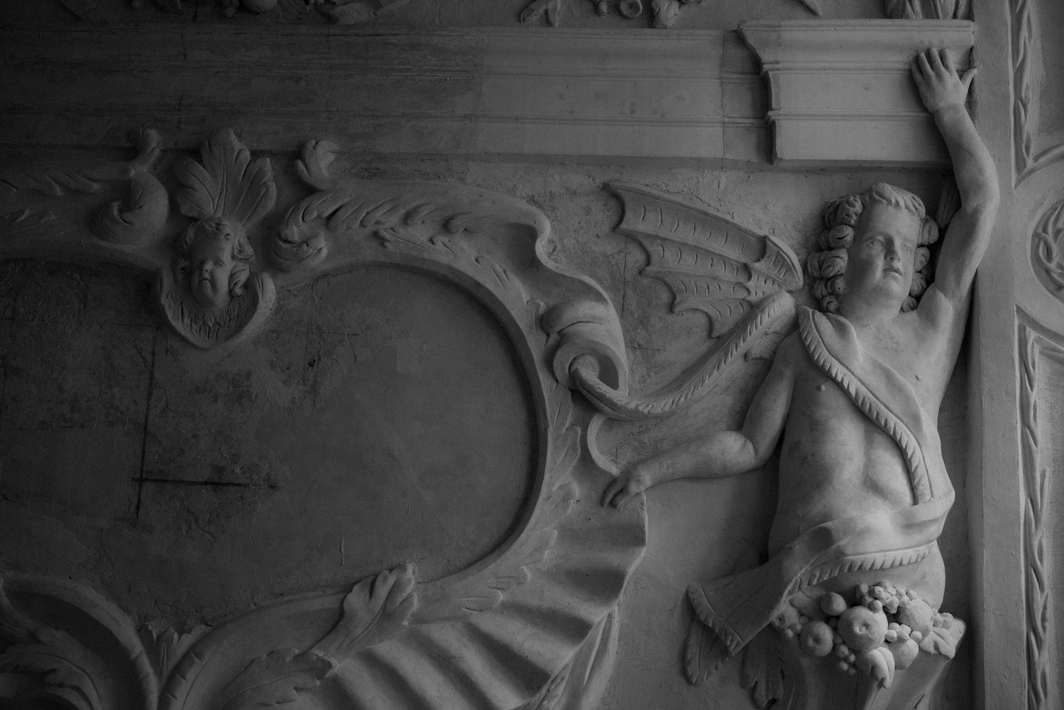 A carved decorative architectural detail featuring an ornate baroque-style figure with flowing elements in black and white.