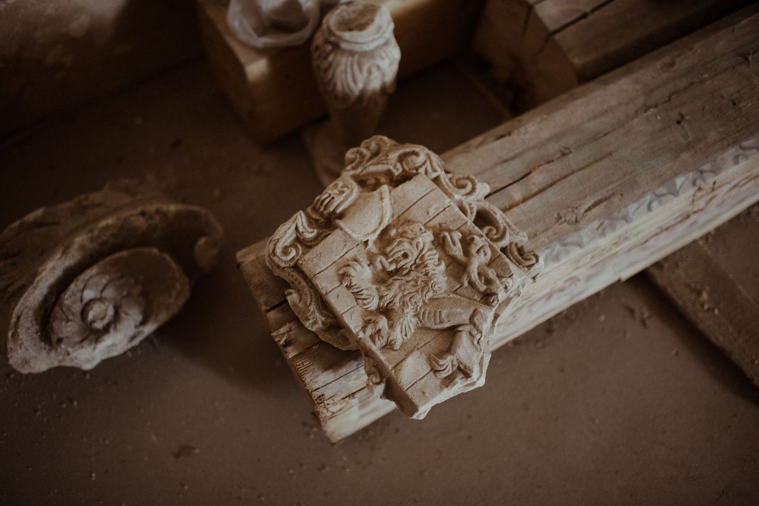 Antique architectural salvage piece showing an ornate carved capital detail in sepia tones on weathered wood surface.