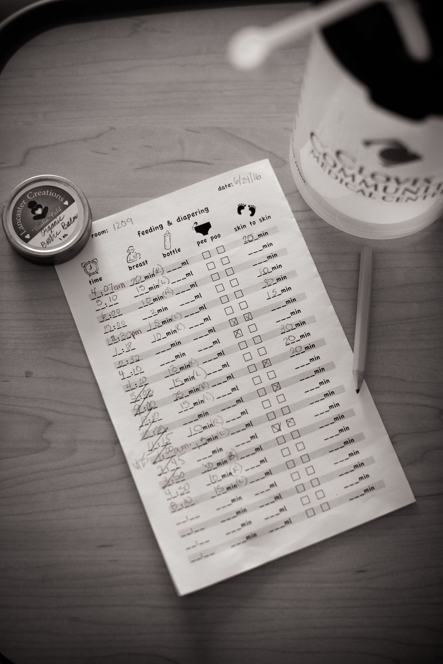 A black and white photograph of a handwritten baby tracker next to a beverage cup on a wooden table.  Fresno Fresh 48 Hospital Photographer