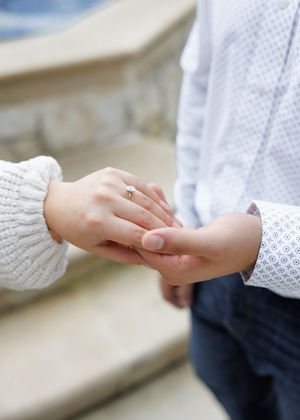 Close-up view of two hands exchanging a ring during a romantic engagement moment.