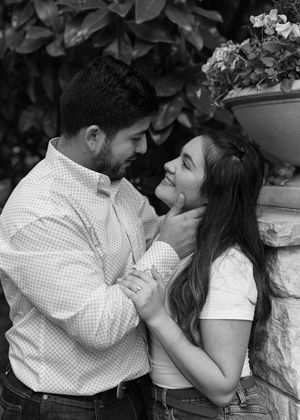 A romantic black and white photo of a couple sharing an intimate moment against a garden backdrop with flowers.