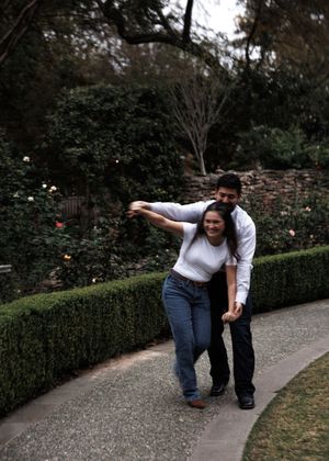 A couple enjoying a playful moment together while walking along a garden path bordered by manicured hedges.