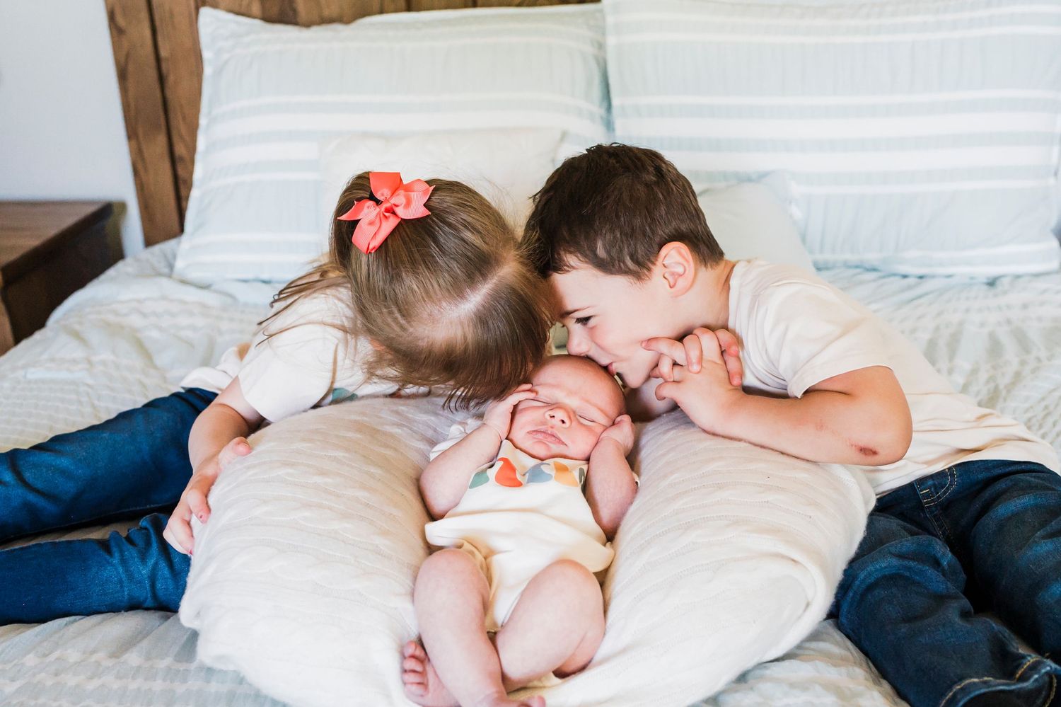 Three siblings cuddle together on a white bed, sharing a sweet moment of connection.