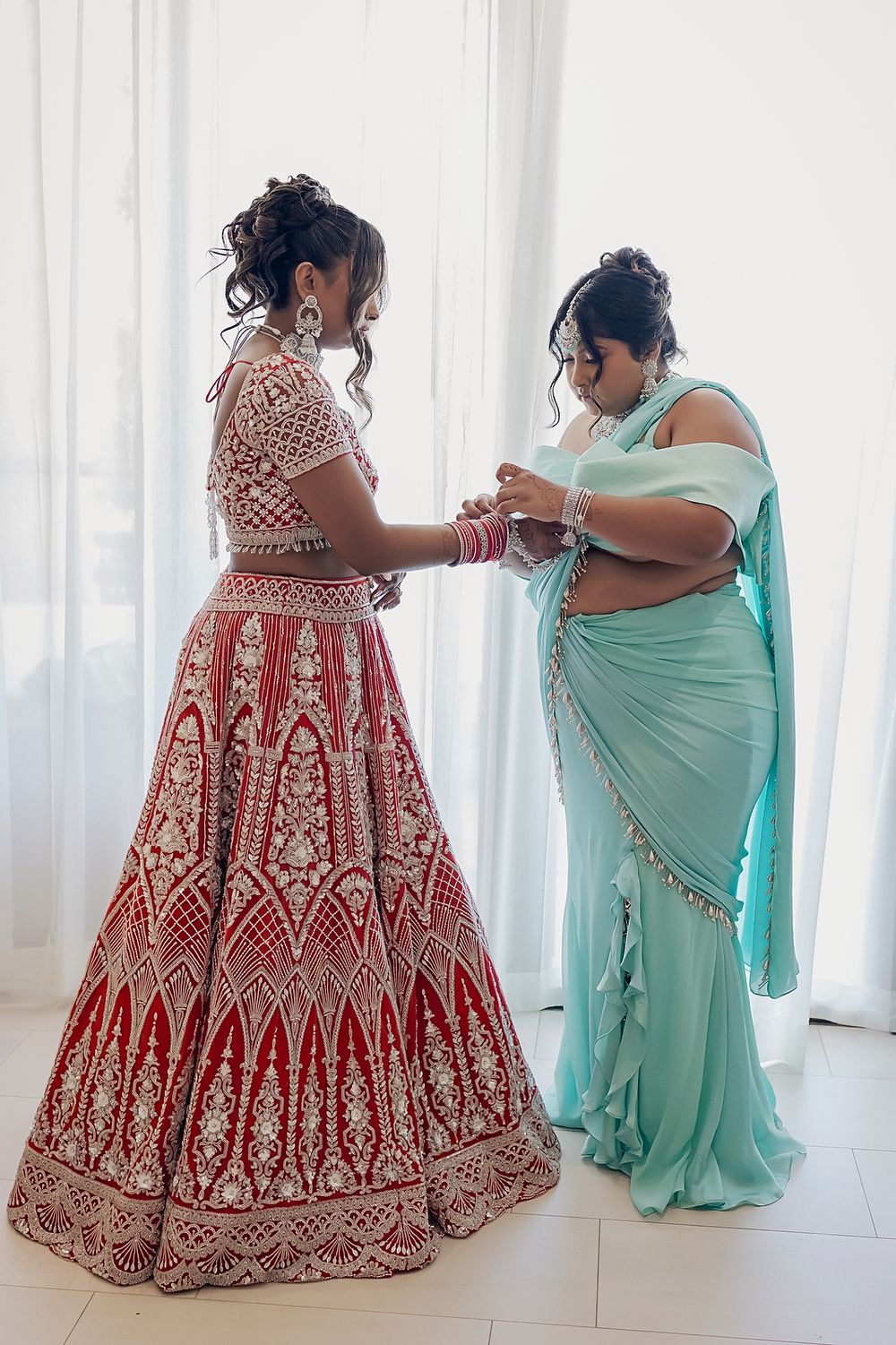Traditional Indian wedding preparation with red lehenga and mint green sari garments being fitted.