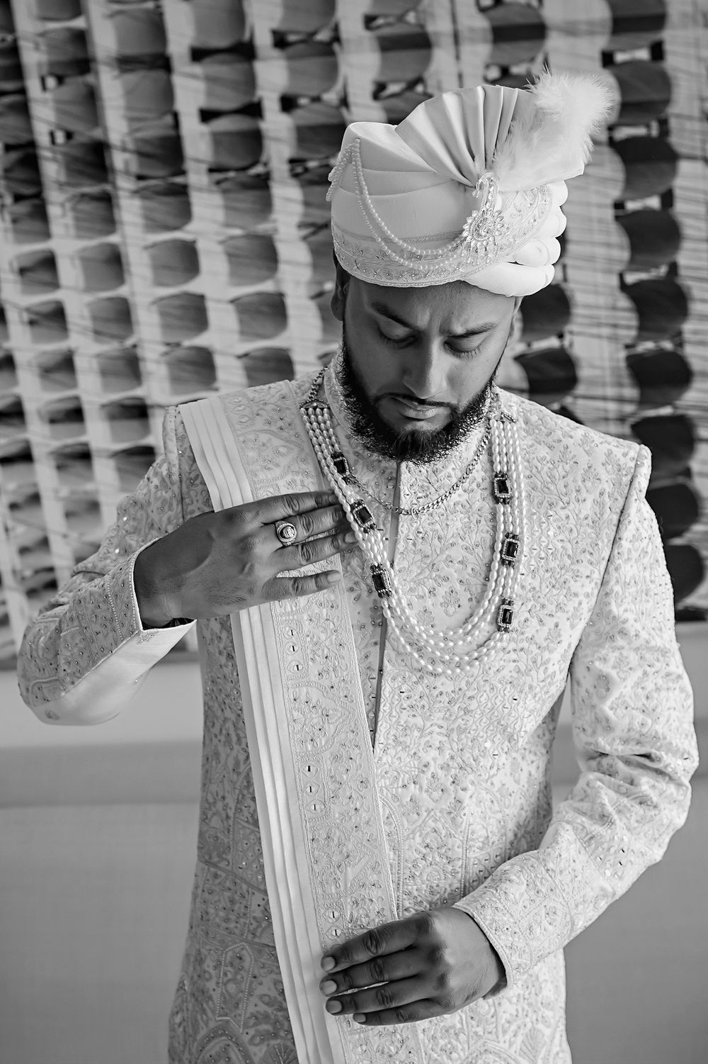 Traditional South Asian groom wearing an ornate white sherwani with intricate embroidery, layered necklaces and turban.