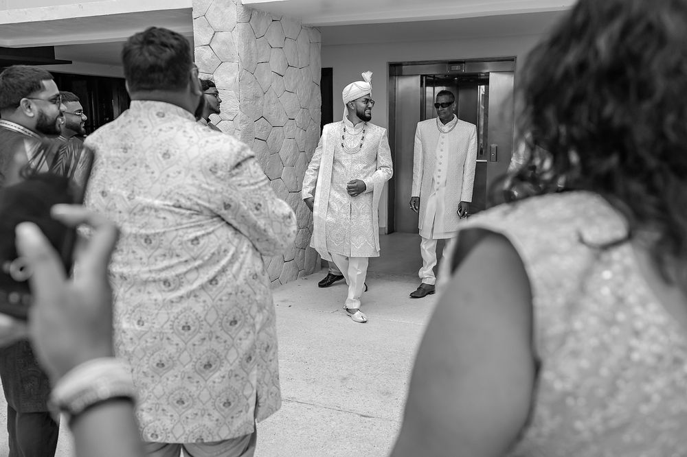 Wedding photographers capture guests in white attire walking together at an elegant indoor venue in black and white.