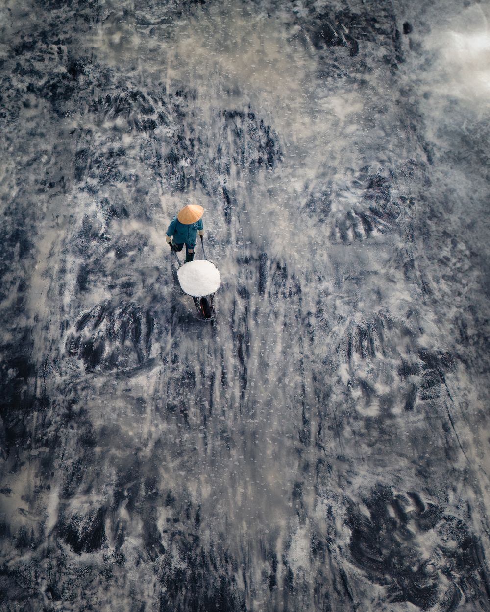 Aerial view of two people holding colorful umbrellas walking on a textured gray surface.