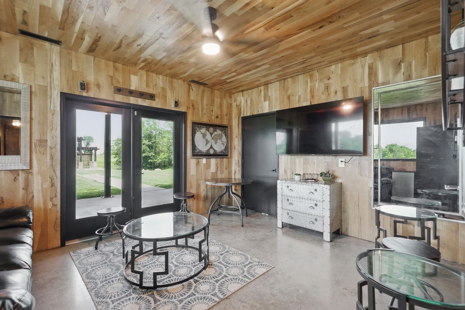 Modern living room with wood paneled walls, glass doors, and round coffee tables on a patterned area rug.