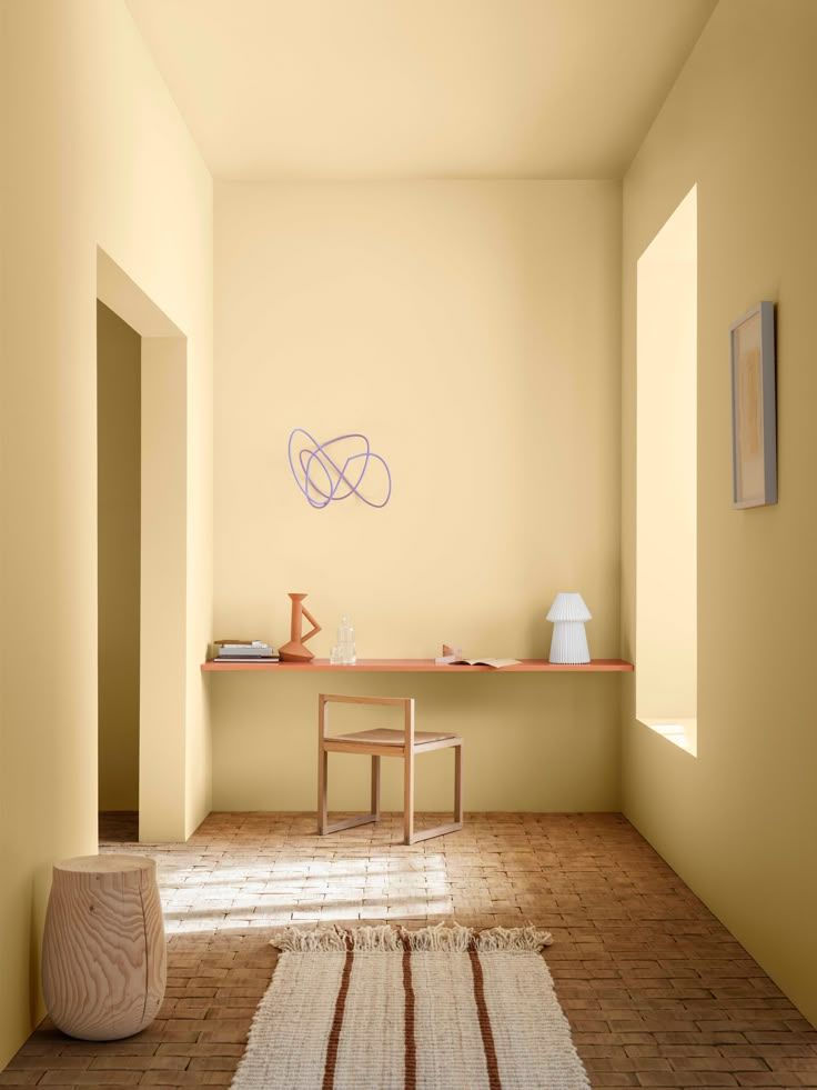 Minimalist room interior with terracotta floor tiles, wooden desk, and geometric wall art in warm natural lighting.