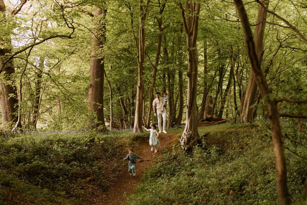 Family walking together on a wooded trail surrounded by lush green trees.