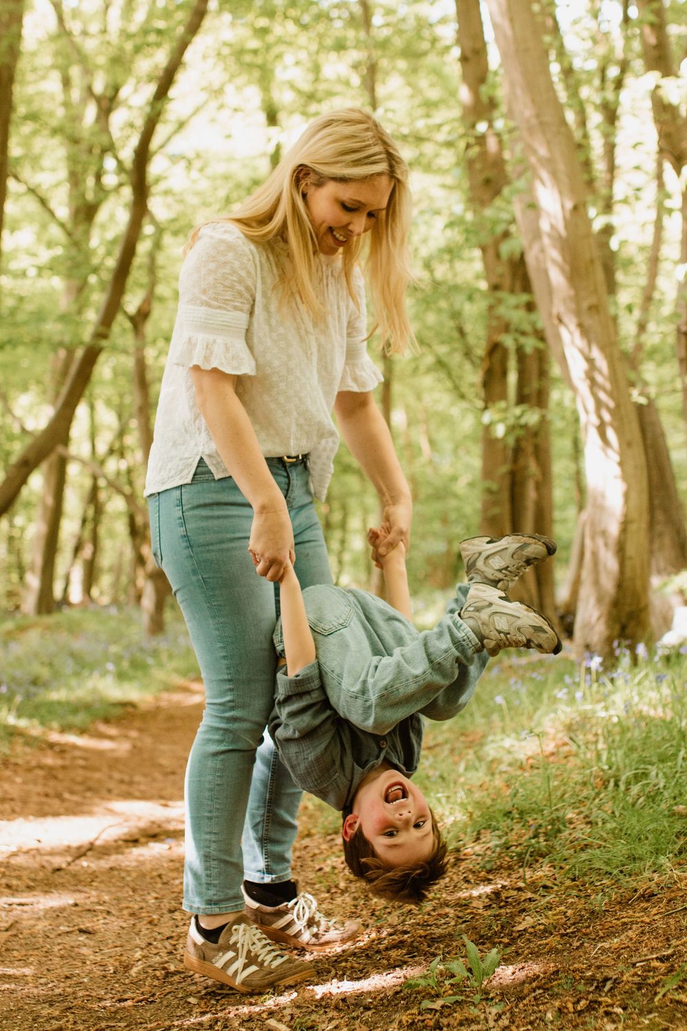 Playful moment on a forest trail with someone being held upside down while laughing.