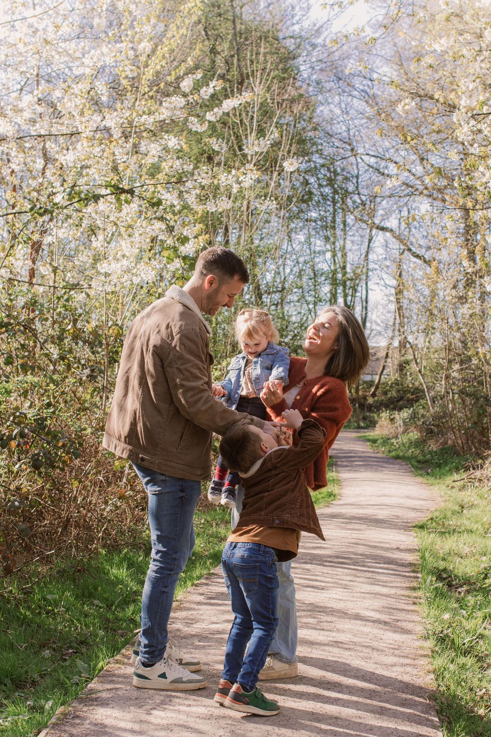 Family enjoying a walk together on a sunny path through blooming trees.