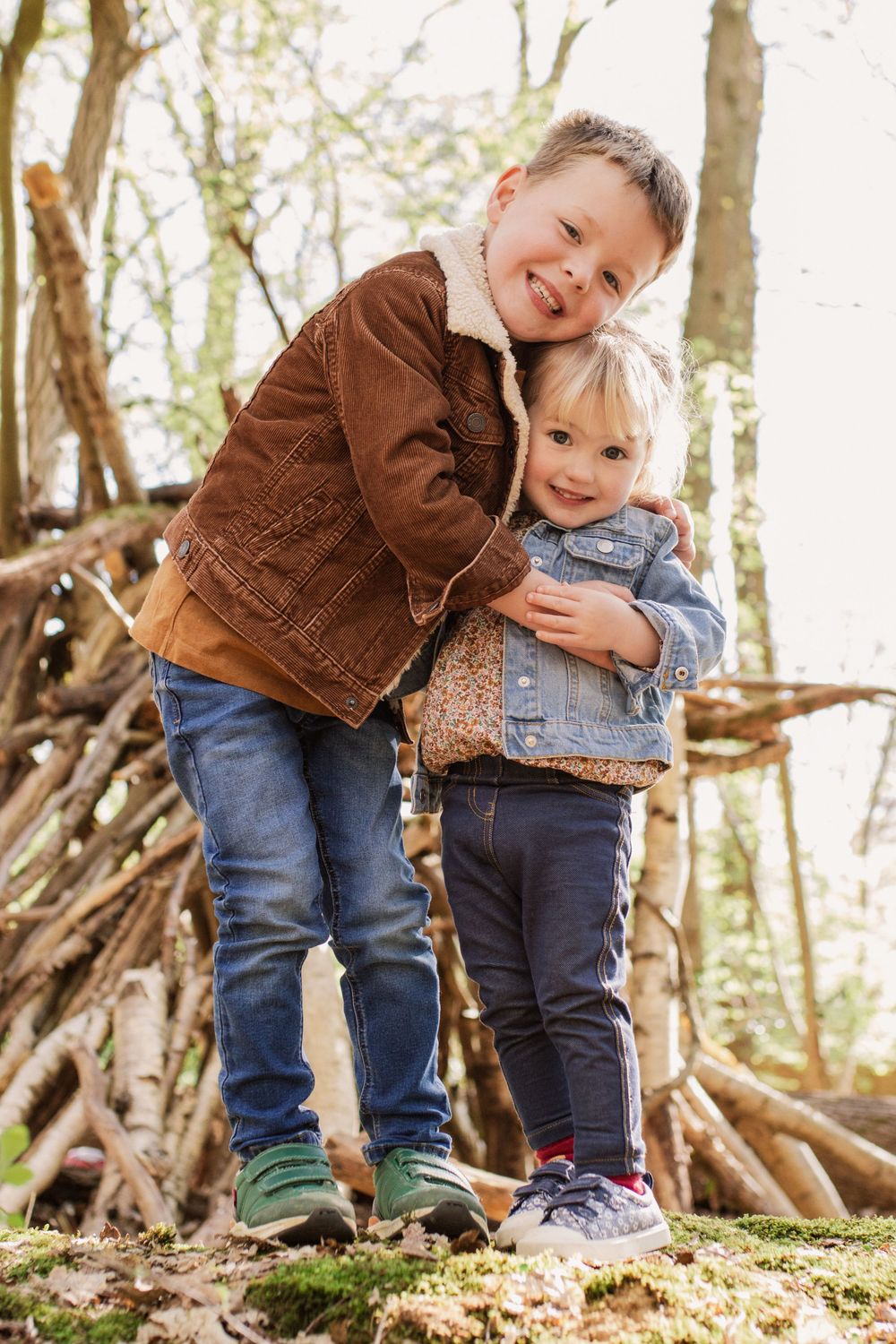 Two small figures explore mossy ground near wooden branches in the woods.