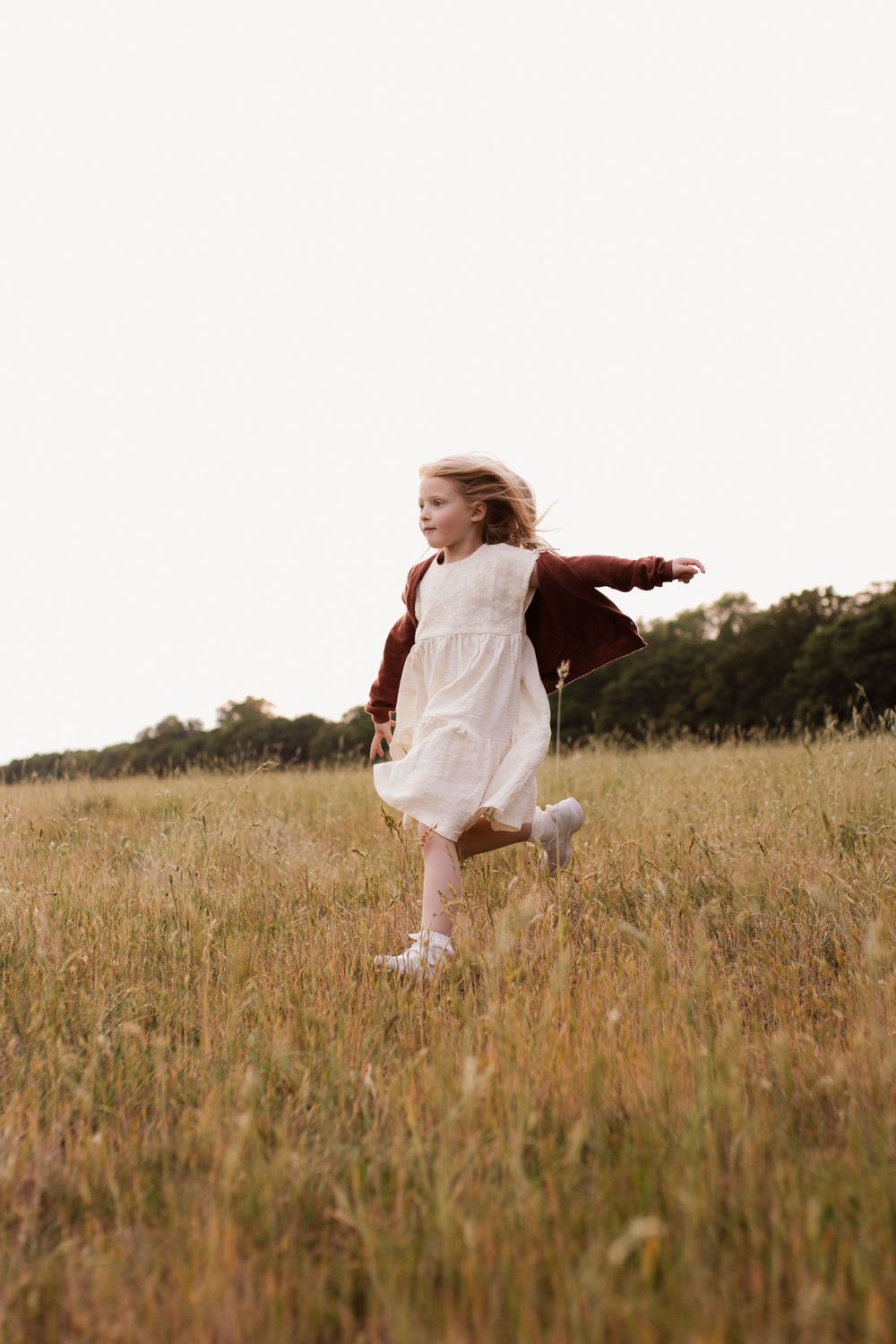 Person in white dress twirling gracefully in a golden field at sunset.