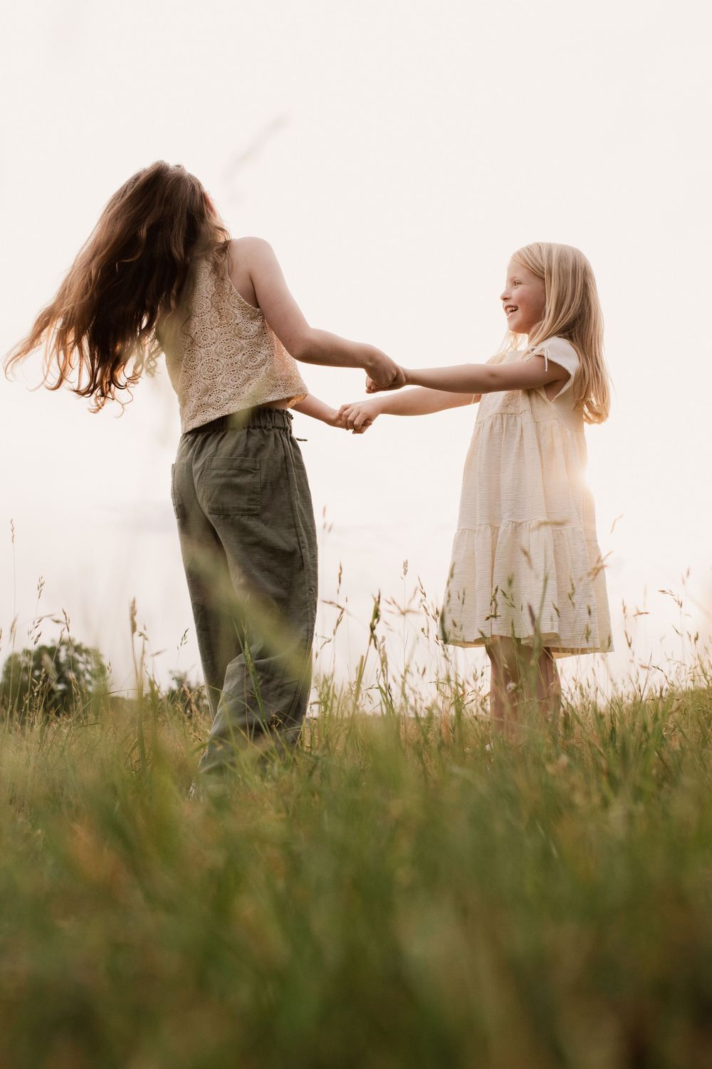 Two people holding hands and spinning together in a sunlit meadow.